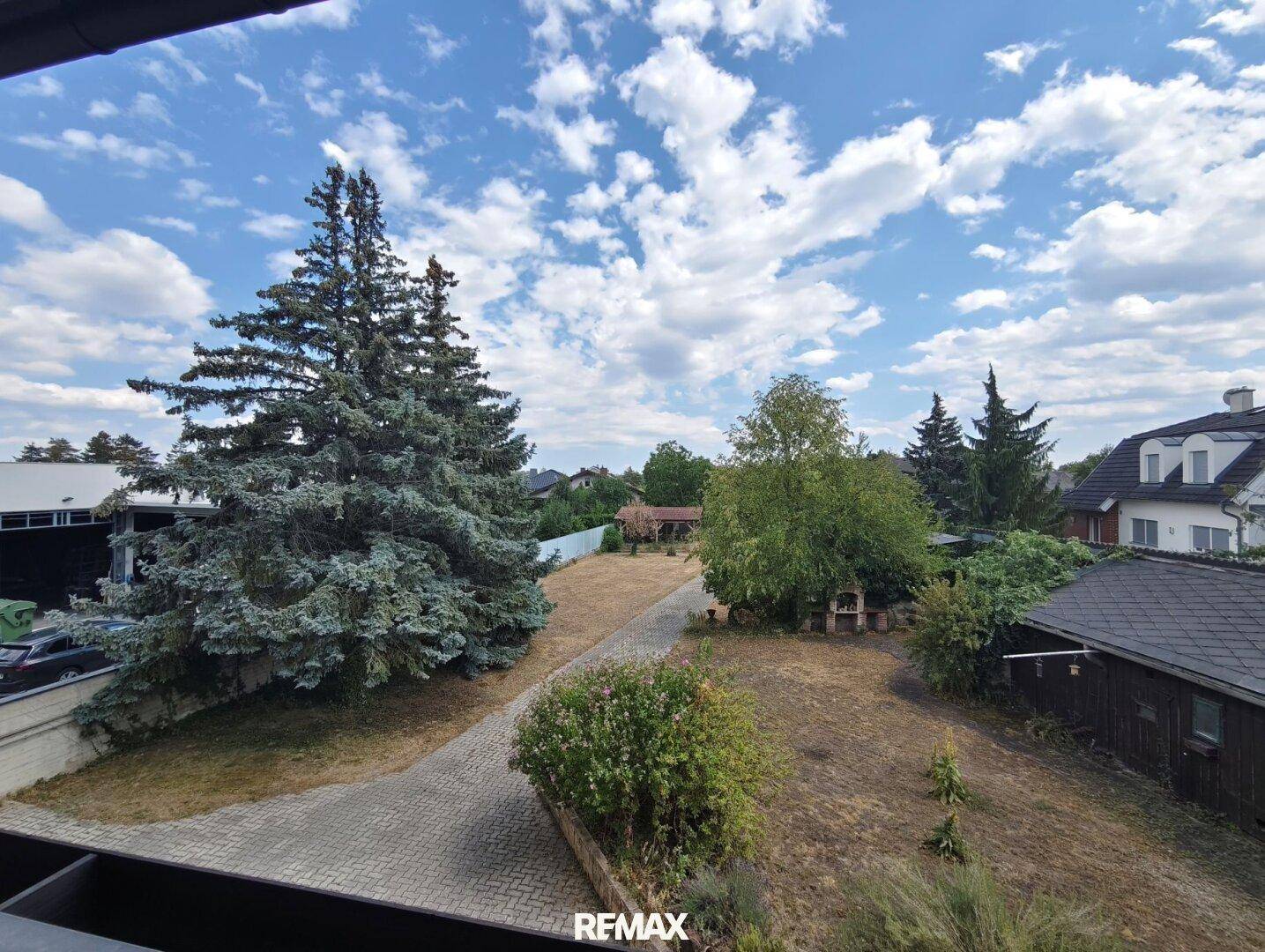Blick vom Balkon über den weitläufigen Garten mit Bäumen und angrenzenden Grundstücken.