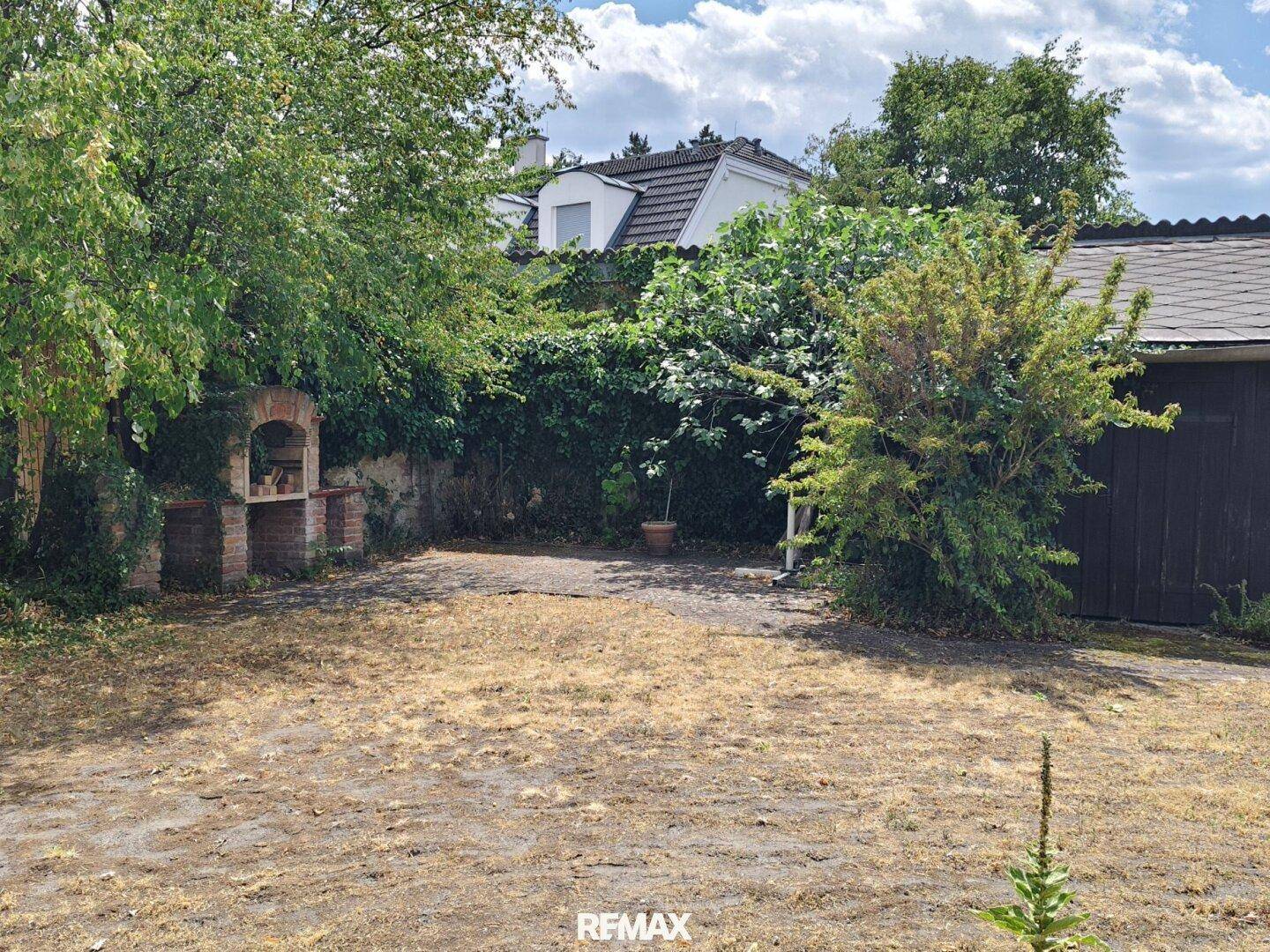 Gartenbereich mit Rasenfläche, Bäumen und einem gemauerten Grillplatz.