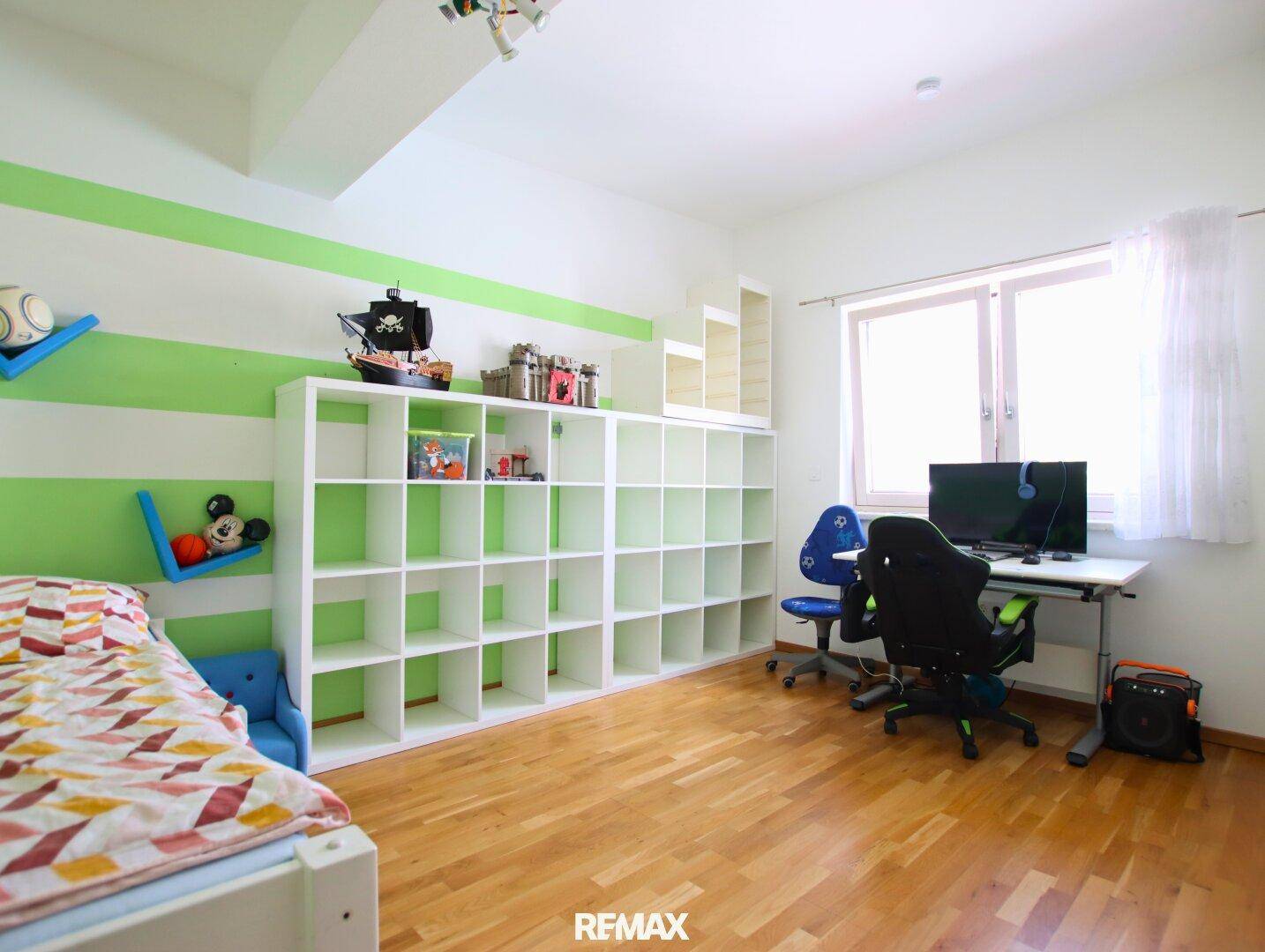 Helles Kinderzimmer mit grün-weiß gestreiften Wänden, Holzboden und großem Regal.