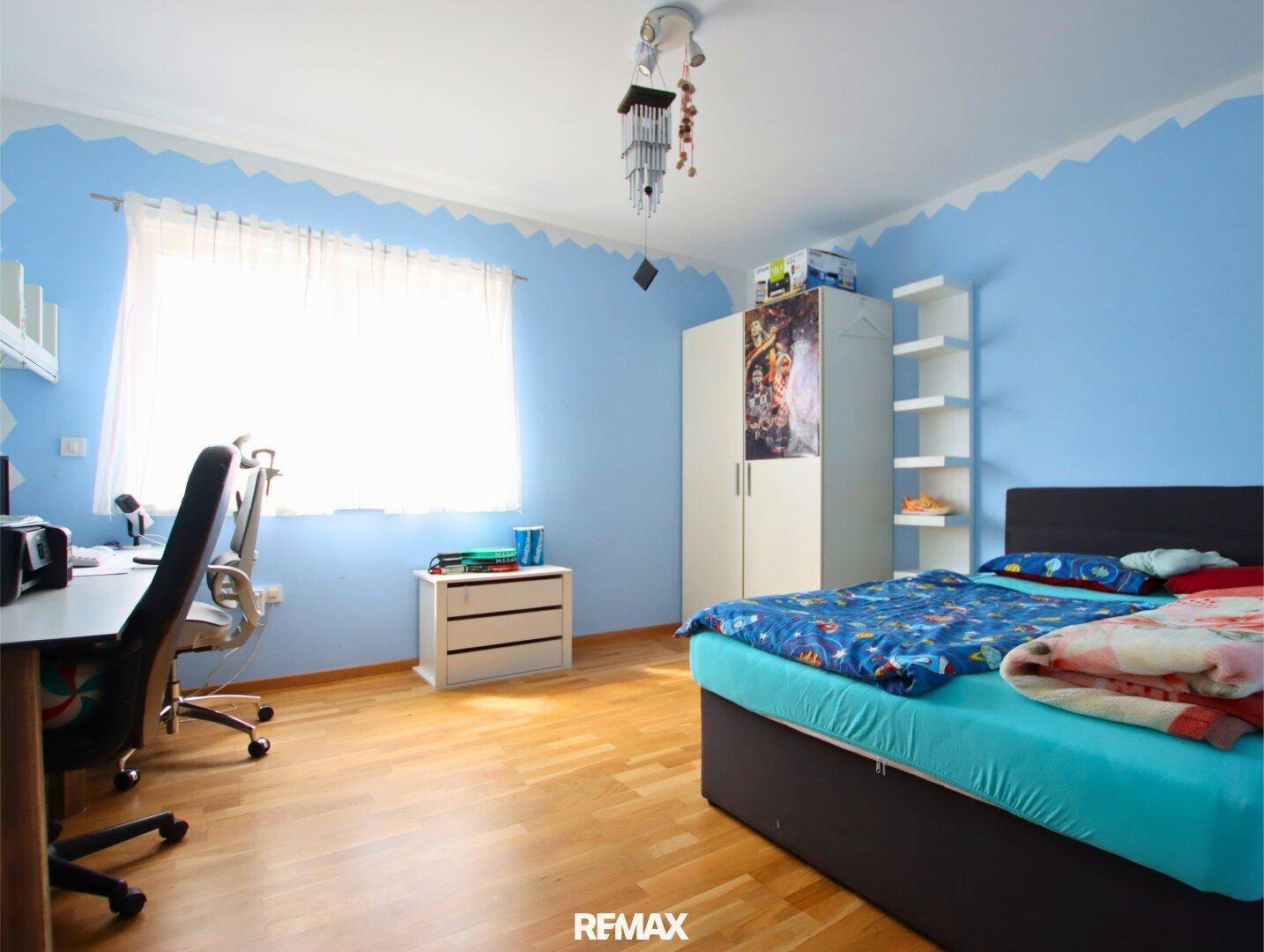 Kinderzimmer mit blau gestrichenen Wänden, Holzboden und Schreibtisch am Fenster.