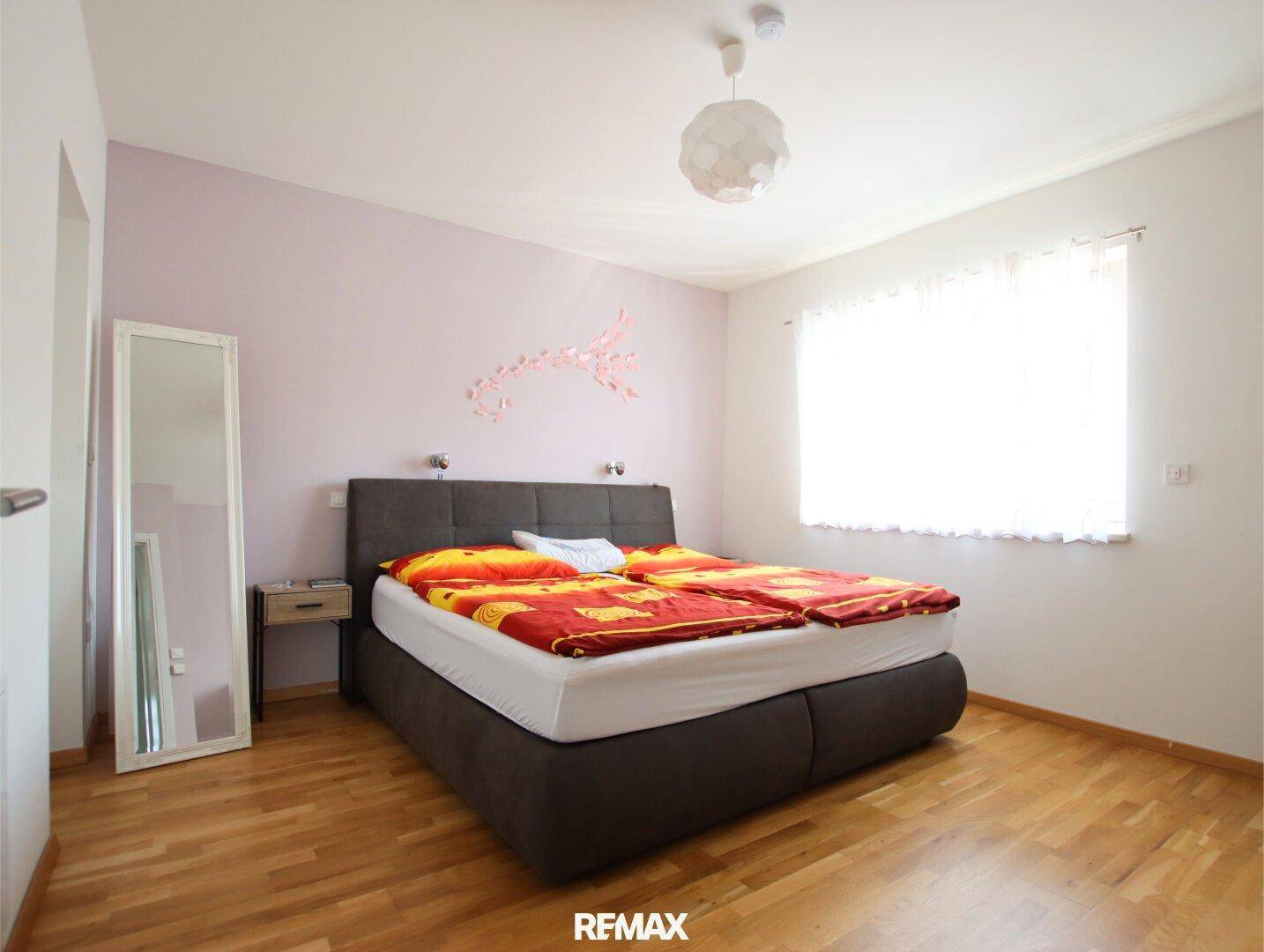 Schlafzimmer mit Doppelbett, Holzboden und hellrosa Wandakzenten.