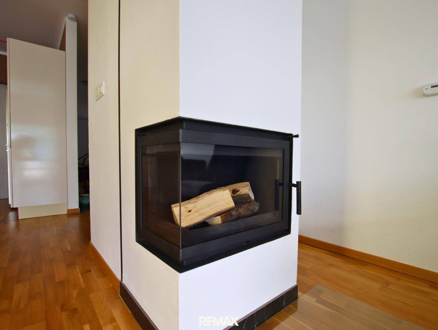 Moderner Eckkamin mit Holzscheiten, integriert in die helle Wohnzimmerwand.
