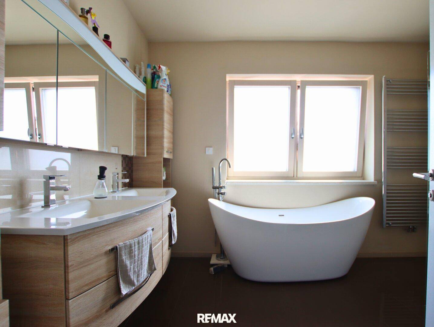 Modernes Badezimmer mit freistehender Badewanne, Doppelwaschbecken und Fenster.