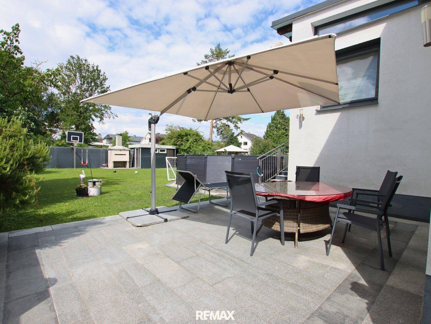Geräumige Terrasse mit Gartenmöbeln, Sonnenschirm und Blick auf den Garten mit Pool.