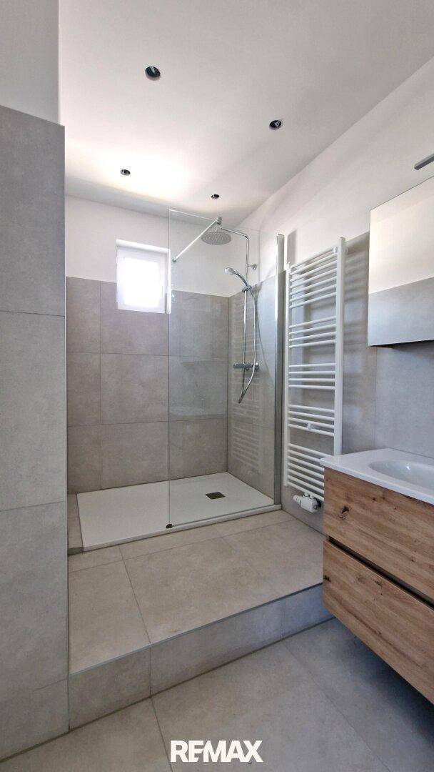 Modernes Badezimmer mit begehbarer Dusche, grauen Fliesen und Handtuchheizkörper.