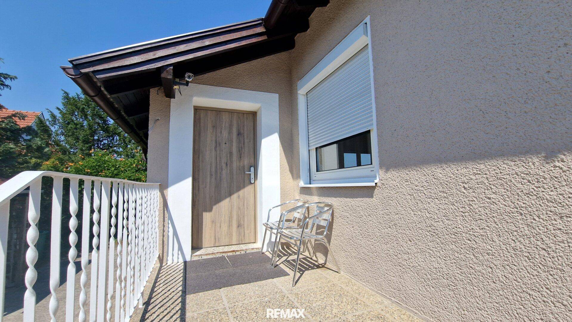 Kleiner Balkon am Hauseingang mit zwei Stühlen und Rollladenfenster.