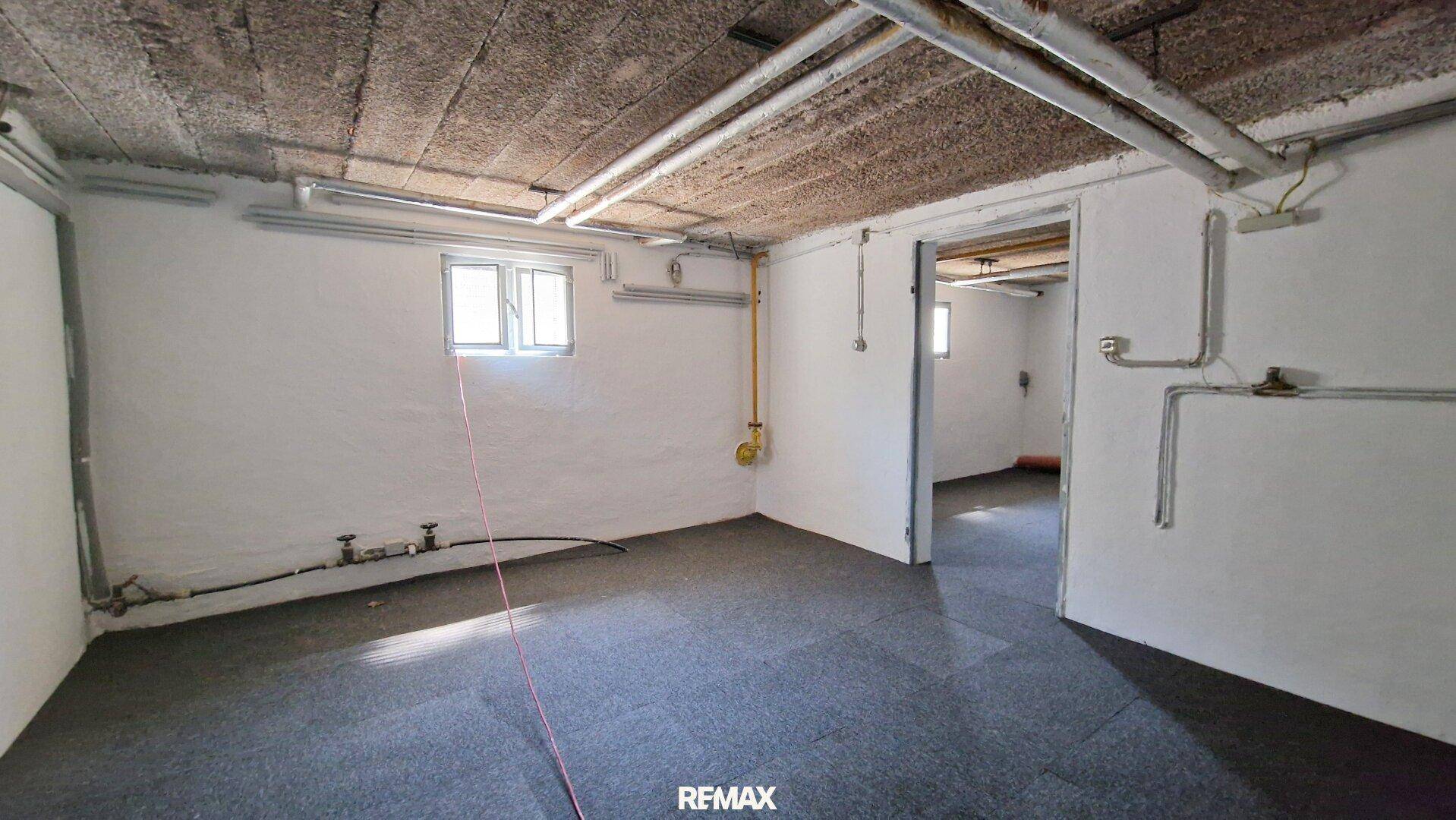 Geräumiger Kellerraum mit Fenstern und sichtbaren Leitungen an der Decke.