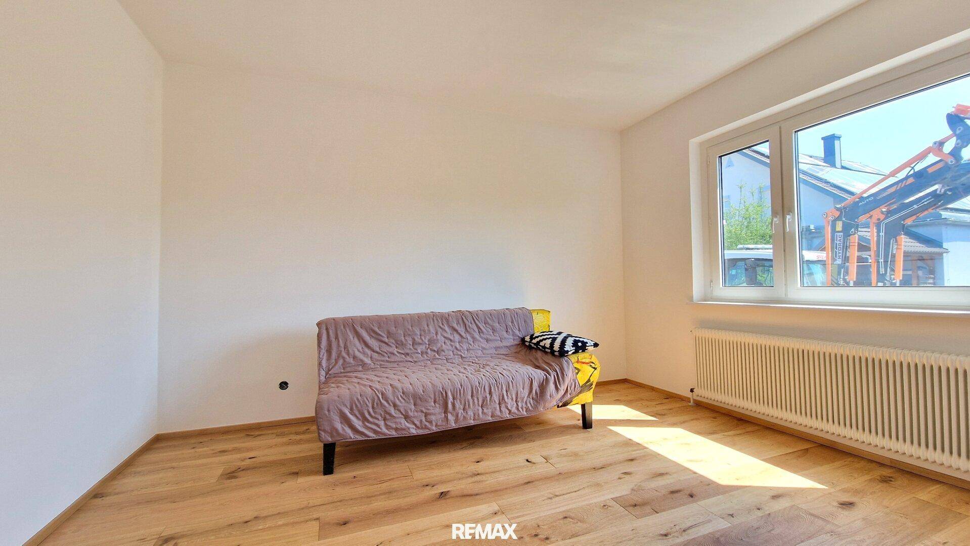 Schlafzimmer mit Holzboden, weiß gestrichenen Wänden und Fenster.
