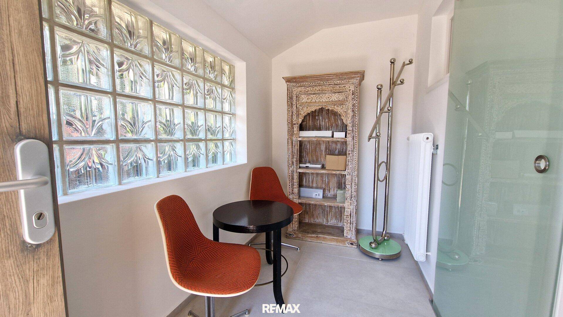 Kleiner Sitzbereich mit Glastisch und dekorativem Regal neben einer Glasbausteinwand.