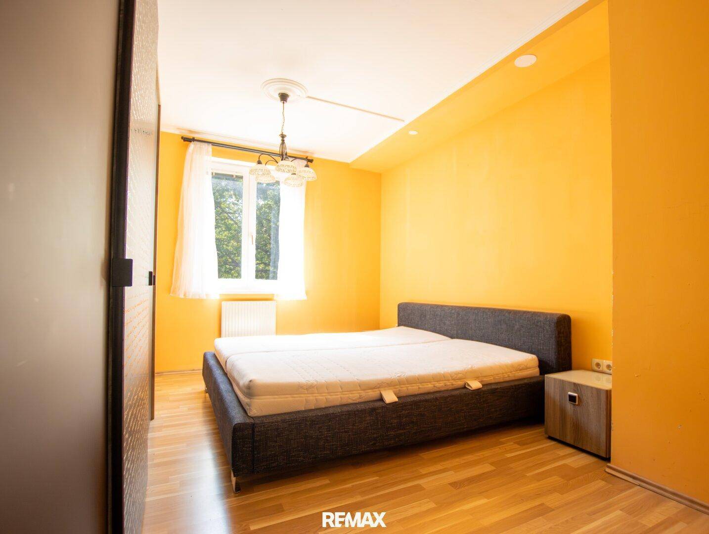 Gemütliches Schlafzimmer mit leuchtend gelben Wänden, Doppelbett und Laminatboden.