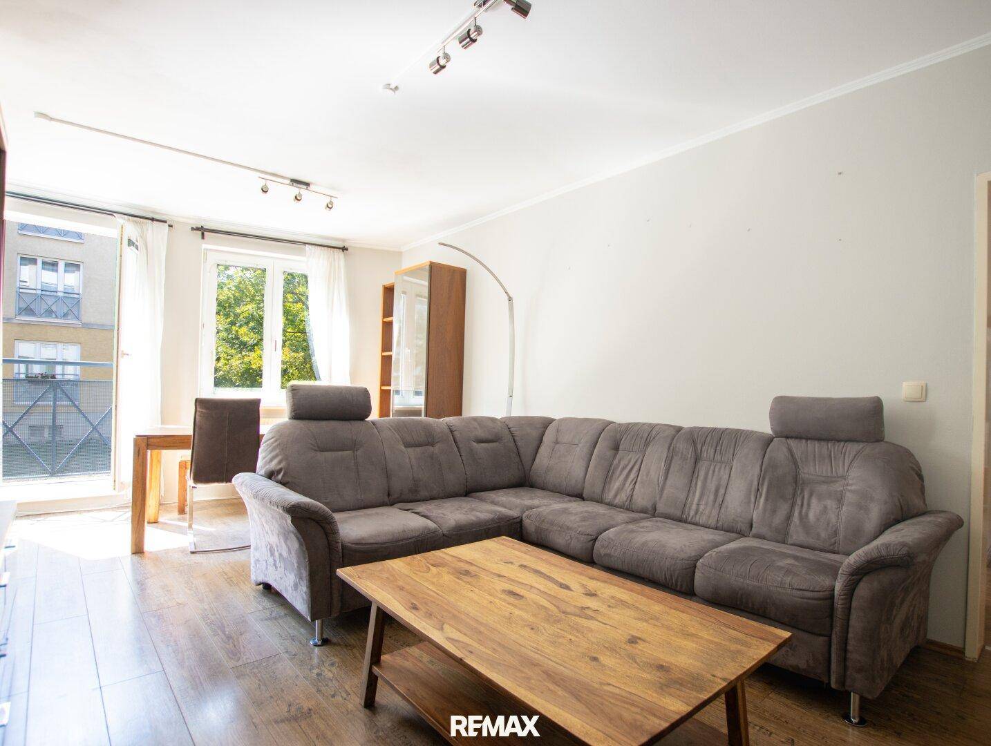 Heller Wohn- und Essbereich mit großem Ecksofa, Holztisch und Zugang zum Balkon.