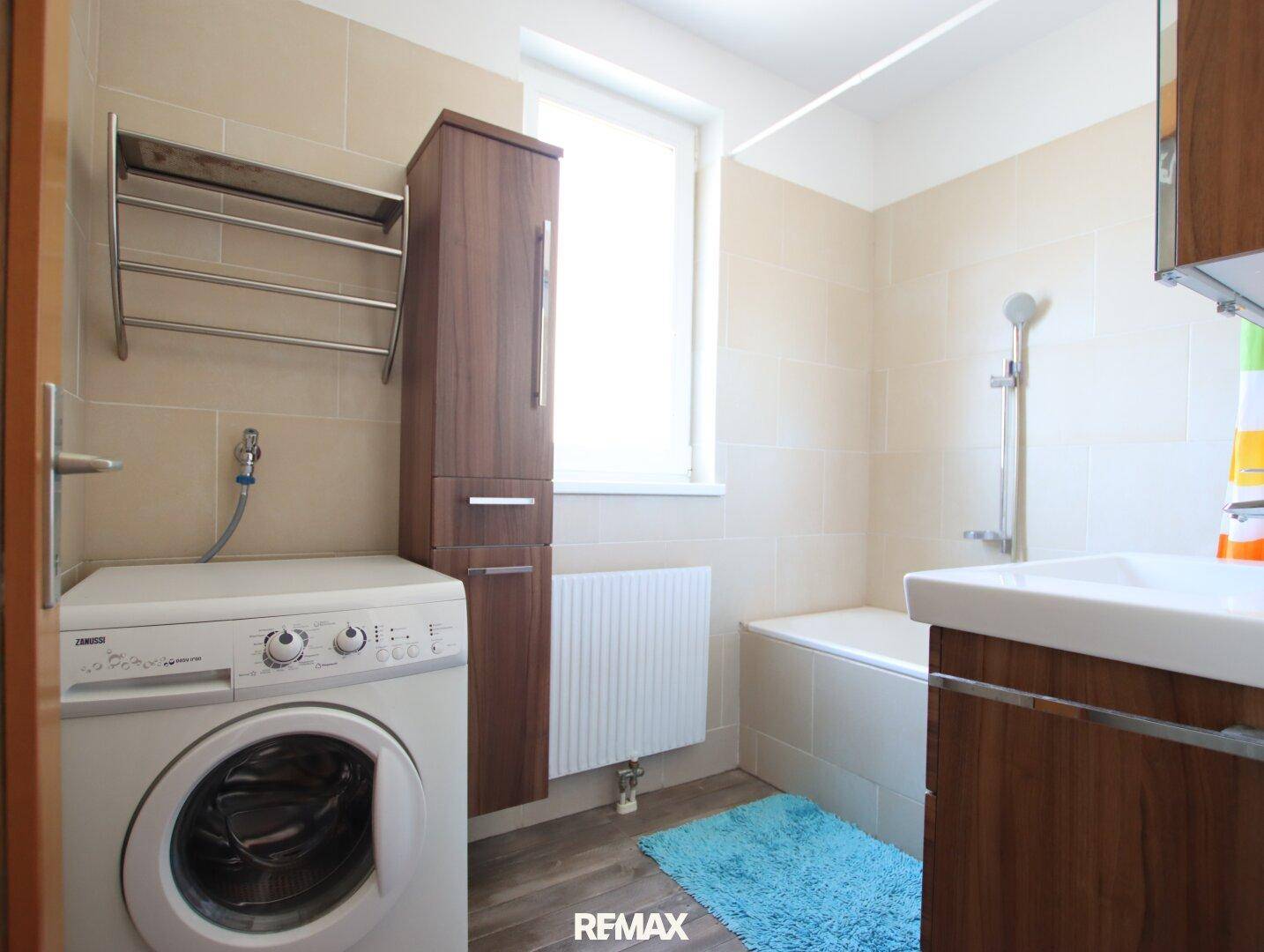 Badezimmer mit Badewanne, Waschmaschine, Waschbecken und Fenster.
