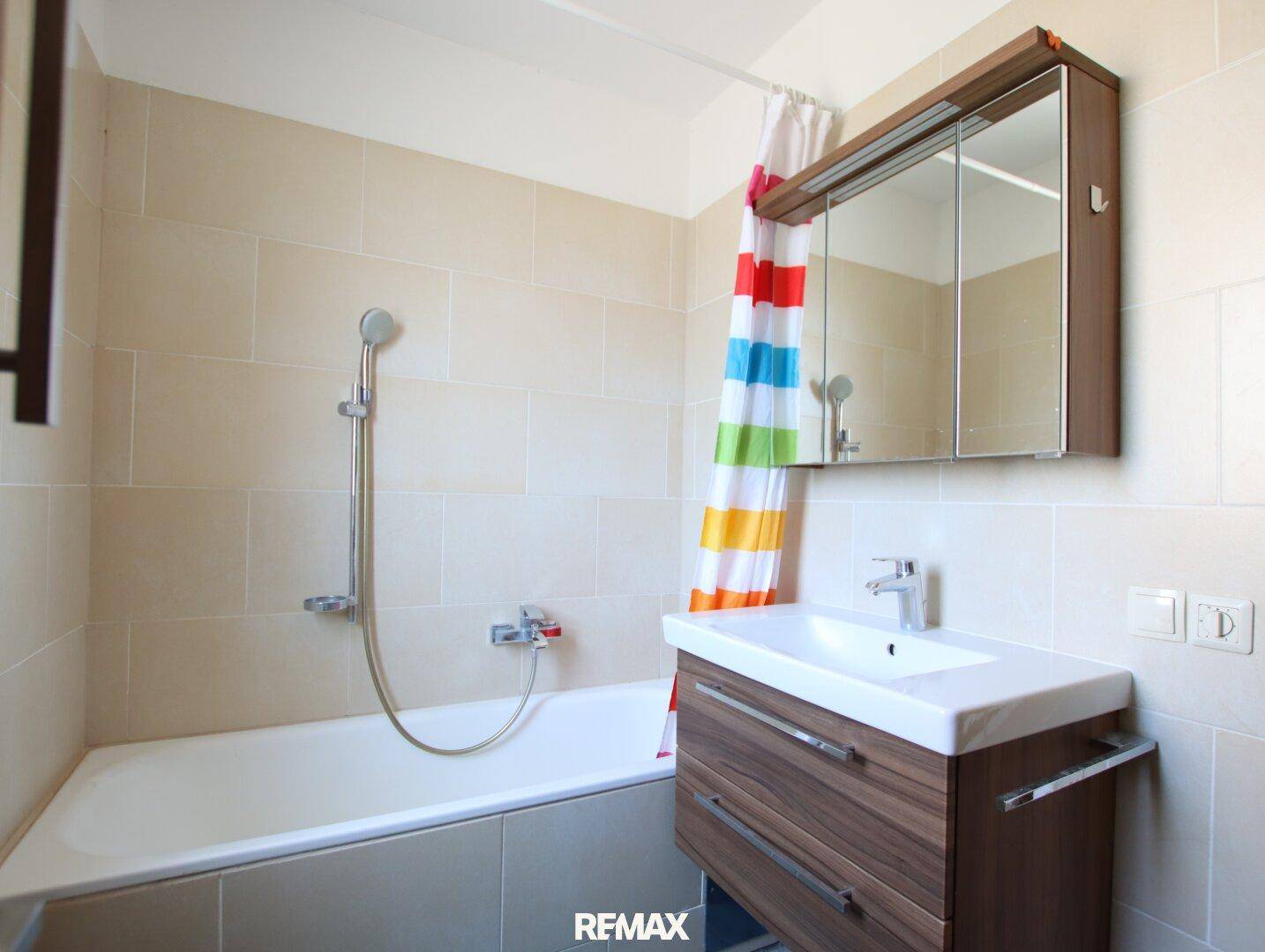 Helles Badezimmer mit Badewanne, Duschvorhang, Waschbecken und Spiegelschrank.