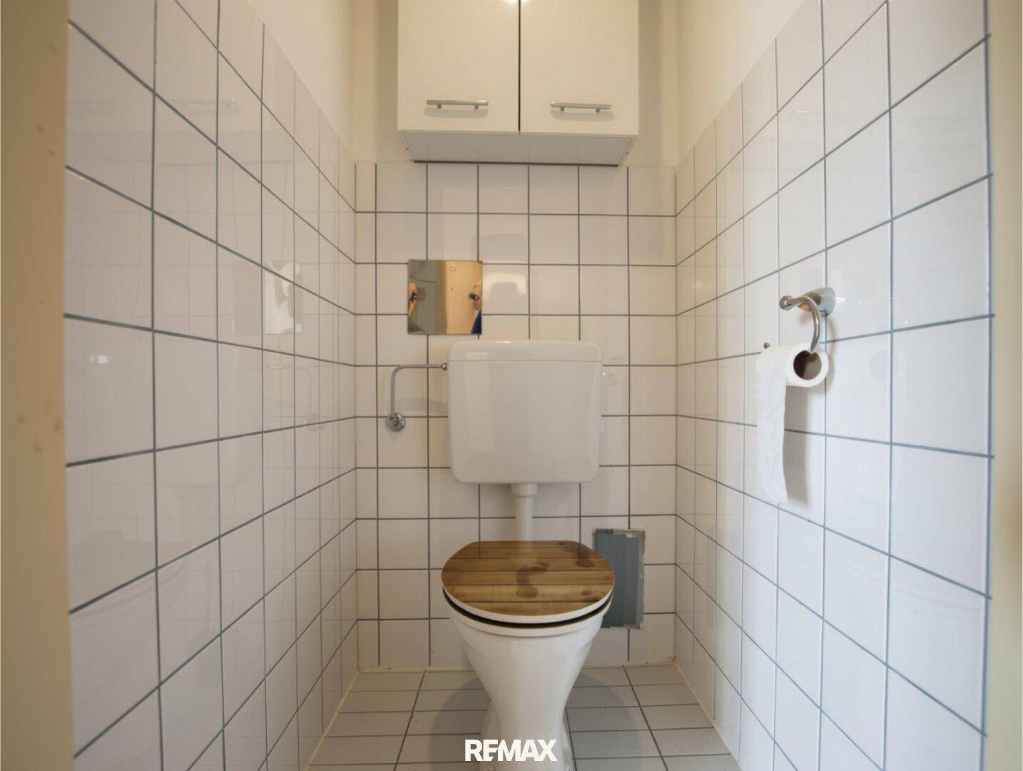 Kleines WC mit weißen Fliesen, Toilette und Holz-Toilettensitz.