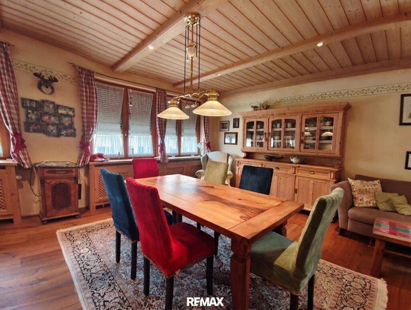 Essbereich im Landhausstil mit großem Holztisch, bunten Stühlen und Holzbalkendecke.
