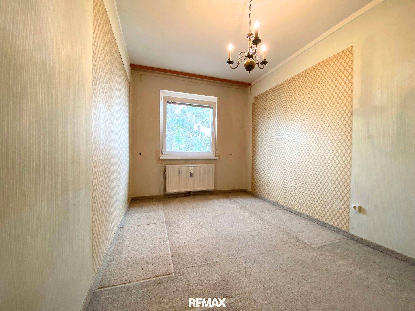 Helles Schlafzimmer mit gemusterter Tapete, Teppichboden und einem Fenster, das Tageslicht hereinlässt.