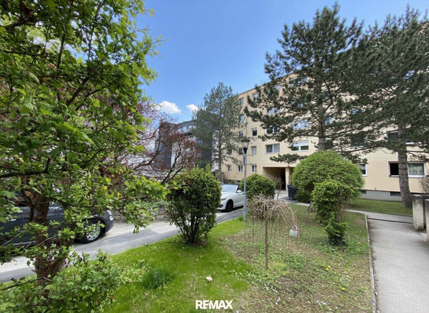 Außenansicht des Wohngebäudes mit gepflegten Grünflächen und Parkmöglichkeiten unter blauem Himmel.