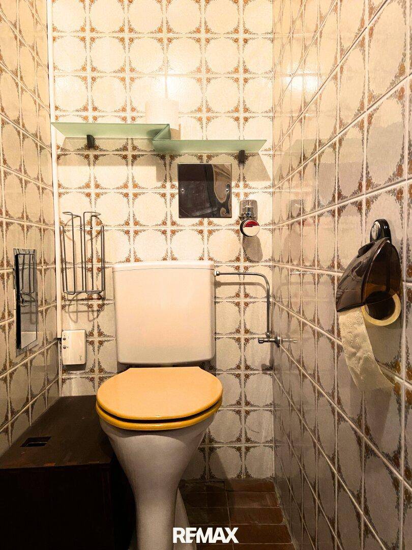 Separate Toilette mit gemusterten Fliesen und einem WC, das eine Renovierung benötigt.