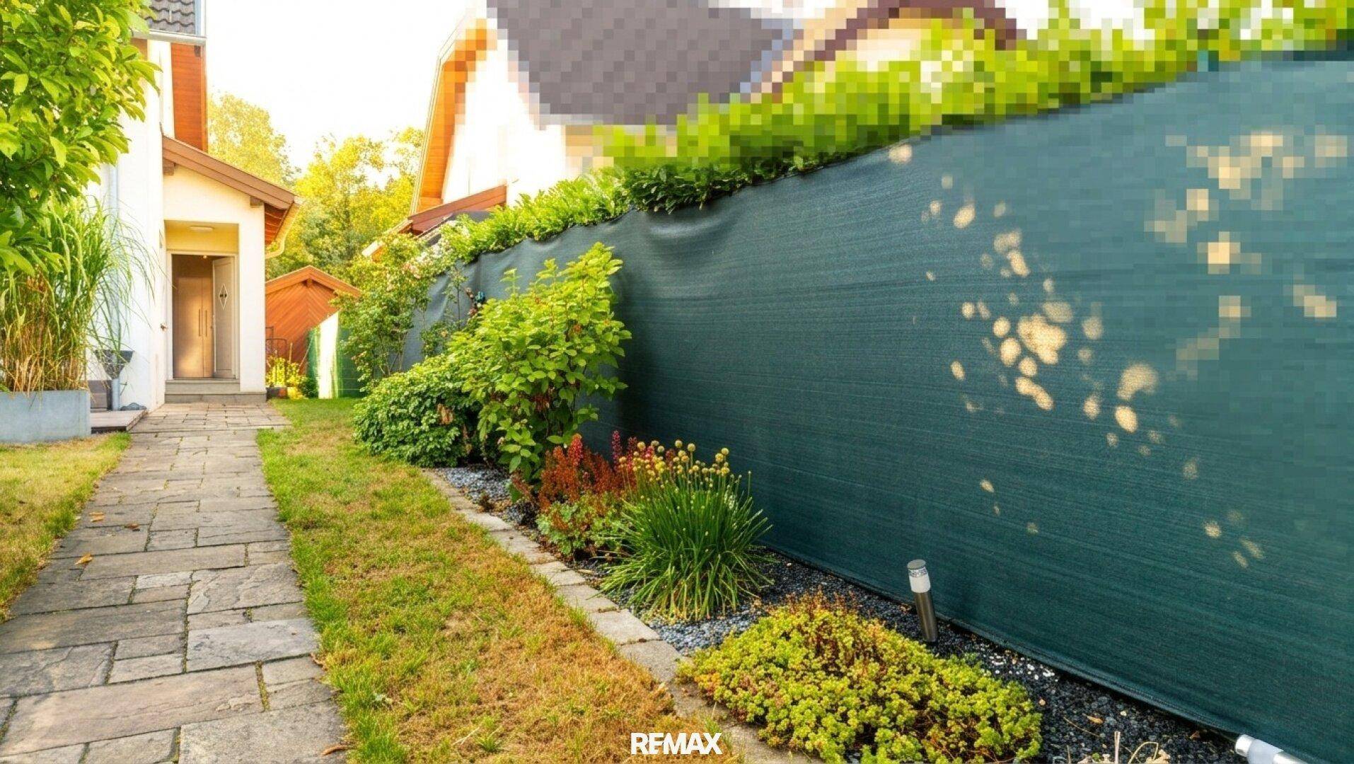 Der Eingangsbereich des Hauses mit einem gepflasterten Weg und einer grünen Sichtschutzwand.