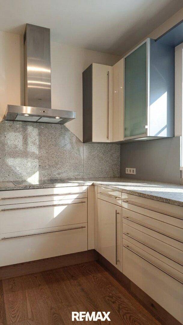 Moderne Küche mit weißen Hochglanzschränken, Granitarbeitsplatte und Dunstabzugshaube.