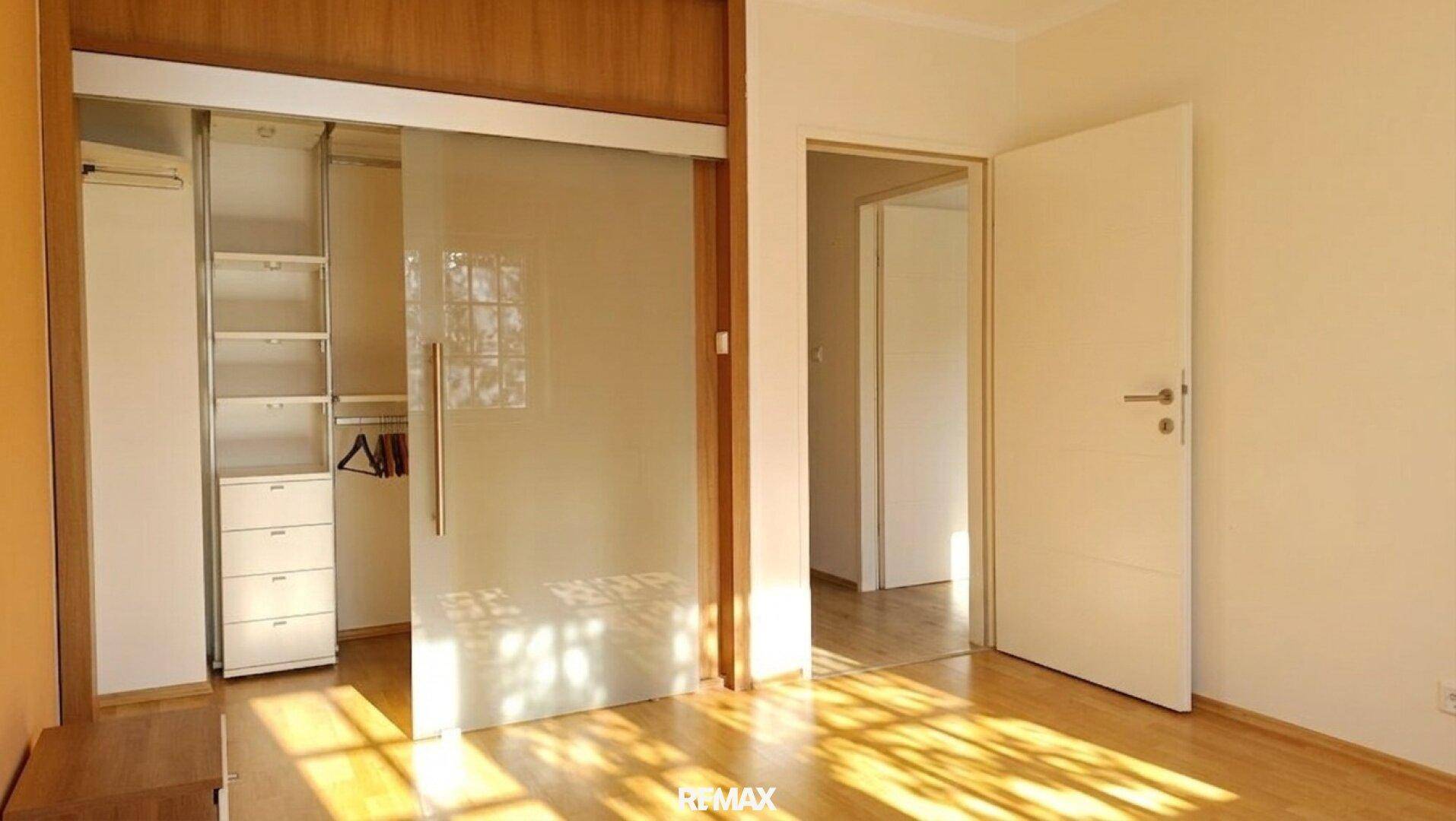 Geräumiges Zimmer mit Holzfußboden und einem begehbaren Kleiderschrank mit Glasschiebetüren.