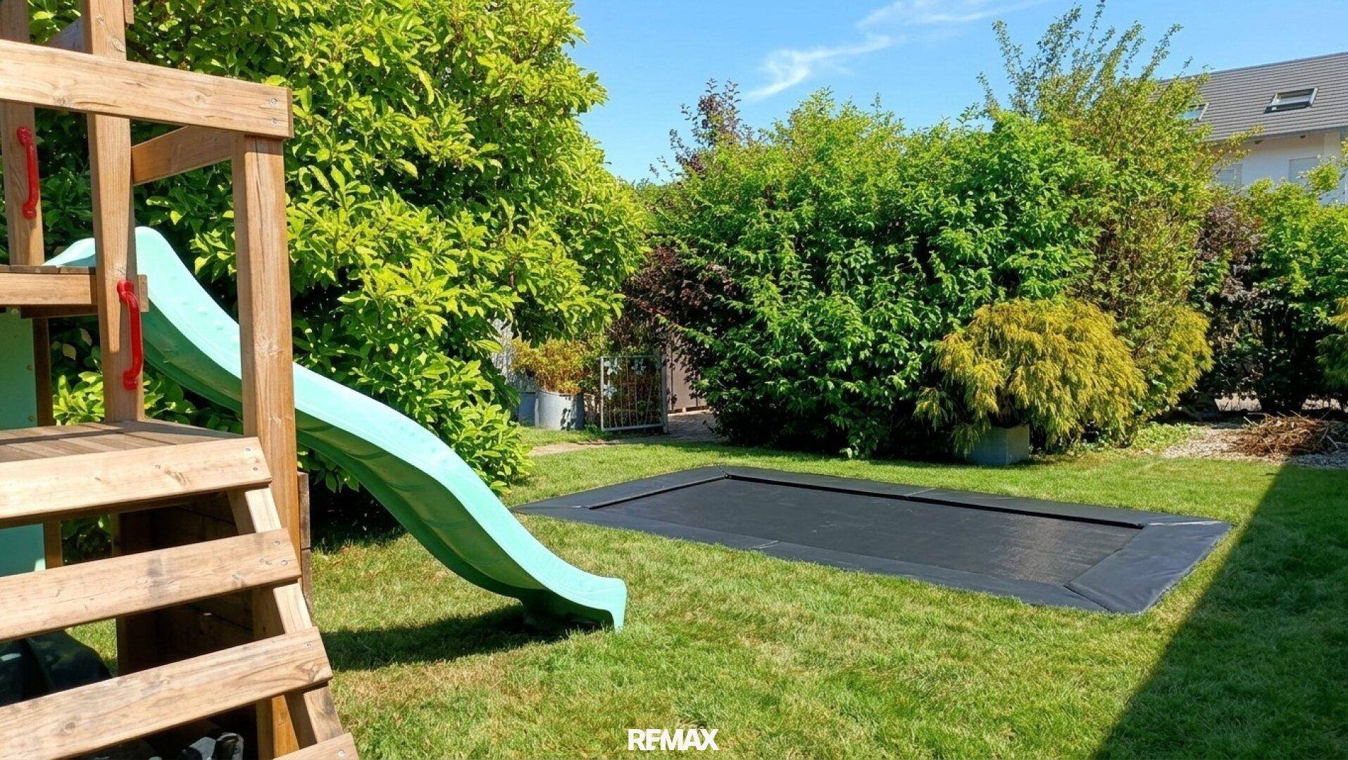 Gepflegter Garten mit Rasenfläche, Spielturm mit Rutsche und einem Bodentrampolin für Kinder.