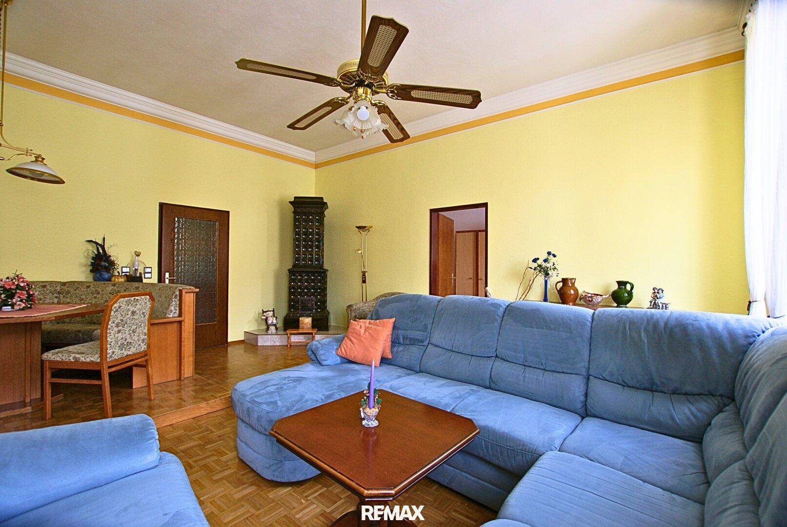 Gemütliches Wohn- und Esszimmer mit Kachelofen, Deckenventilator und traditionellem Parkettboden.