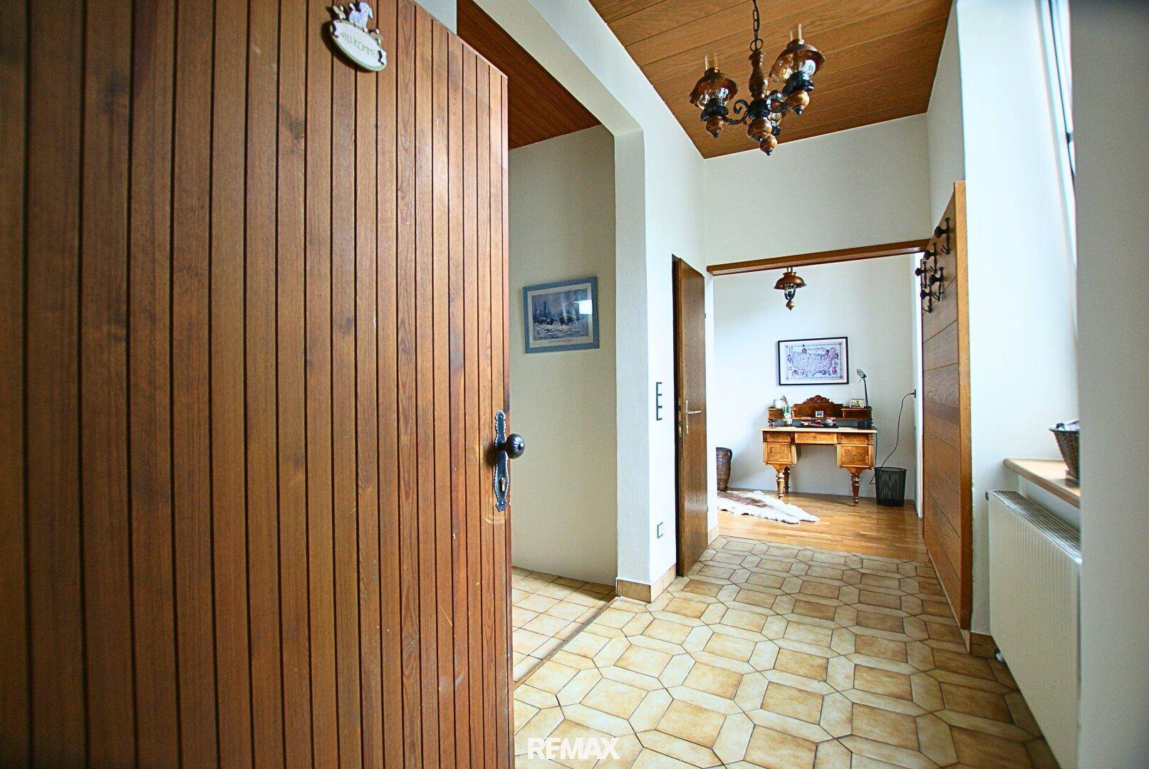 Eingangsbereich mit Holztür, gefliestem Boden und Holzdecke, führt zu weiteren Räumen.