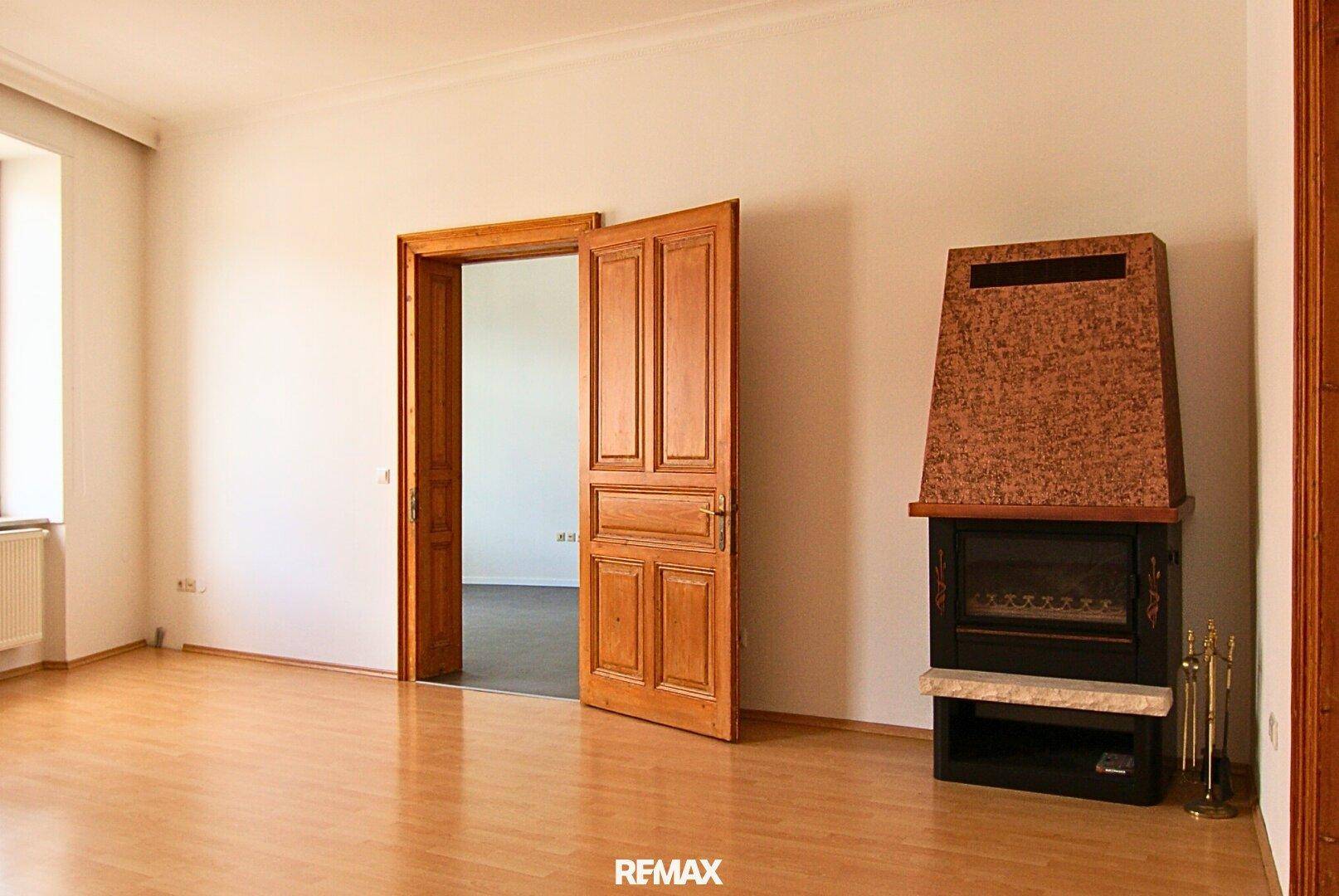 Heller Wohnraum mit Laminatboden, Kamin und einer Doppeltür zu einem weiteren Zimmer.