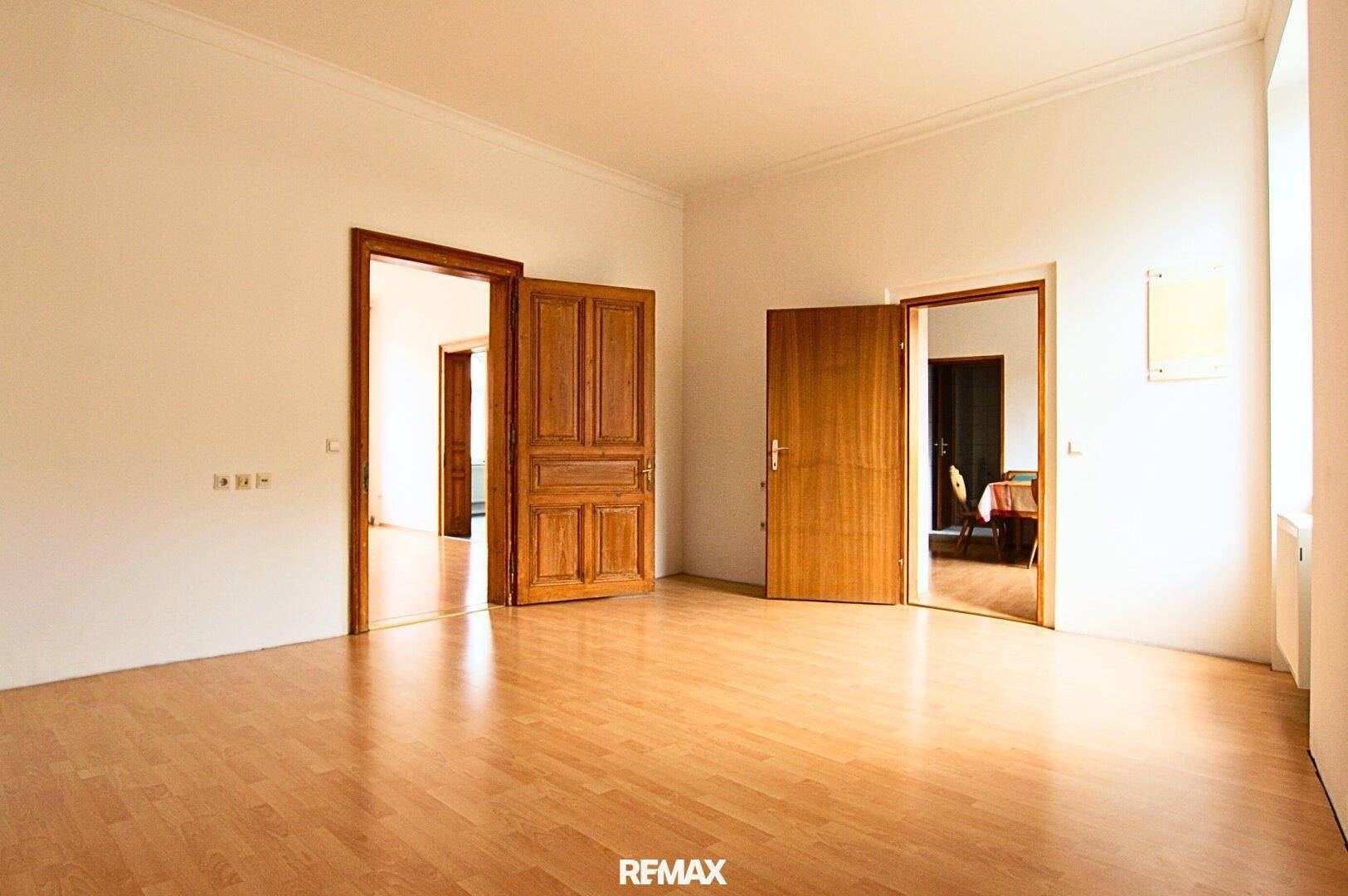 Geräumiger Raum mit Laminatboden, weißen Wänden und mehreren Holztüren zu angrenzenden Zimmern.
