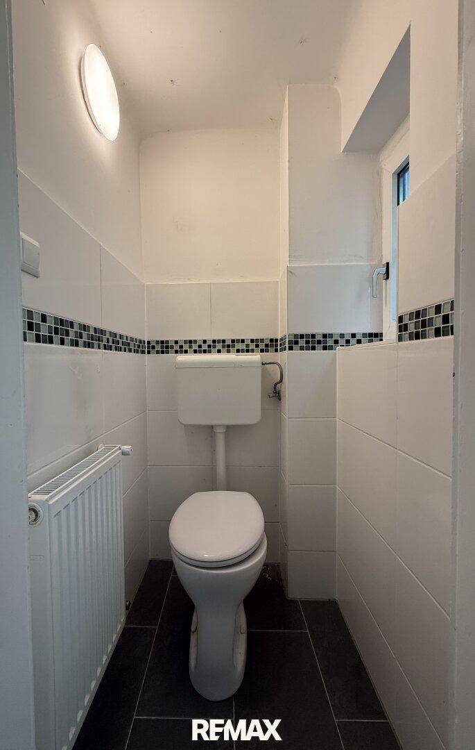 Kleines Gäste-WC mit Toilette, Waschbecken und Fenster, hell gefliest.