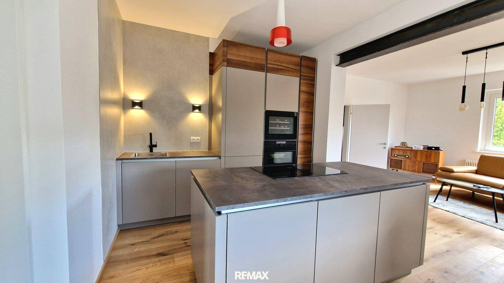 Moderne Küche mit Kochinsel, integrierten Geräten und Holzboden, offen zum Wohnbereich.
