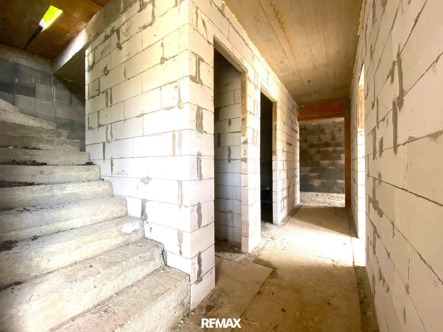Unfertiger Innenraum mit Betontreppe und Rohbauwänden aus hellen Blöcken.