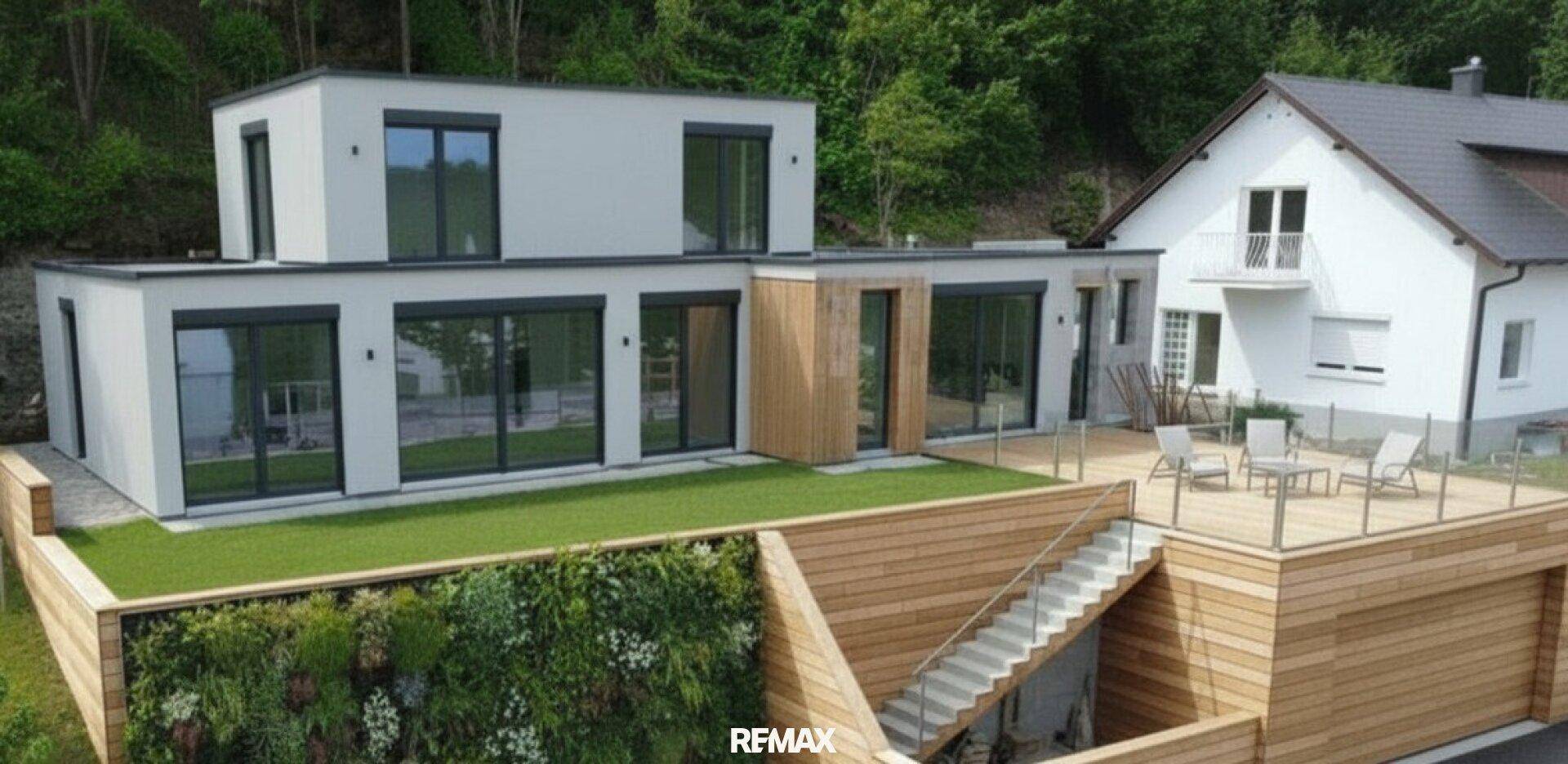 Modernes Haus mit Holzterrasse, Glasgeländer und vertikaler Begrünung, neben einem älteren Gebäude.