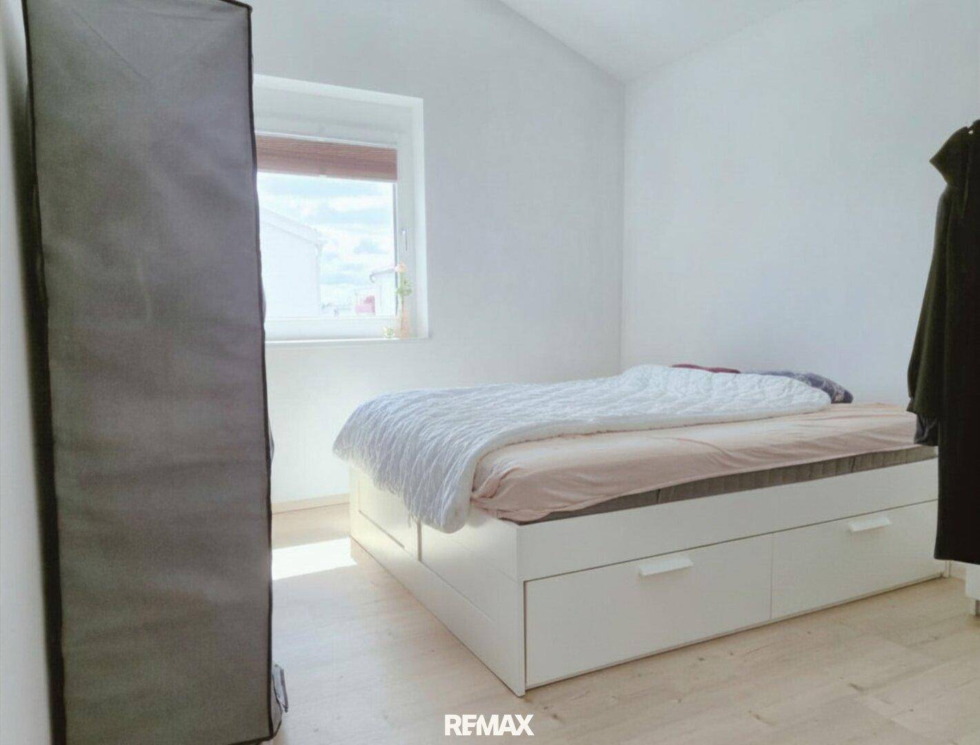 Helles Schlafzimmer mit weiß gestrichenen Wänden, Laminatboden und einem Bett mit Stauraum.