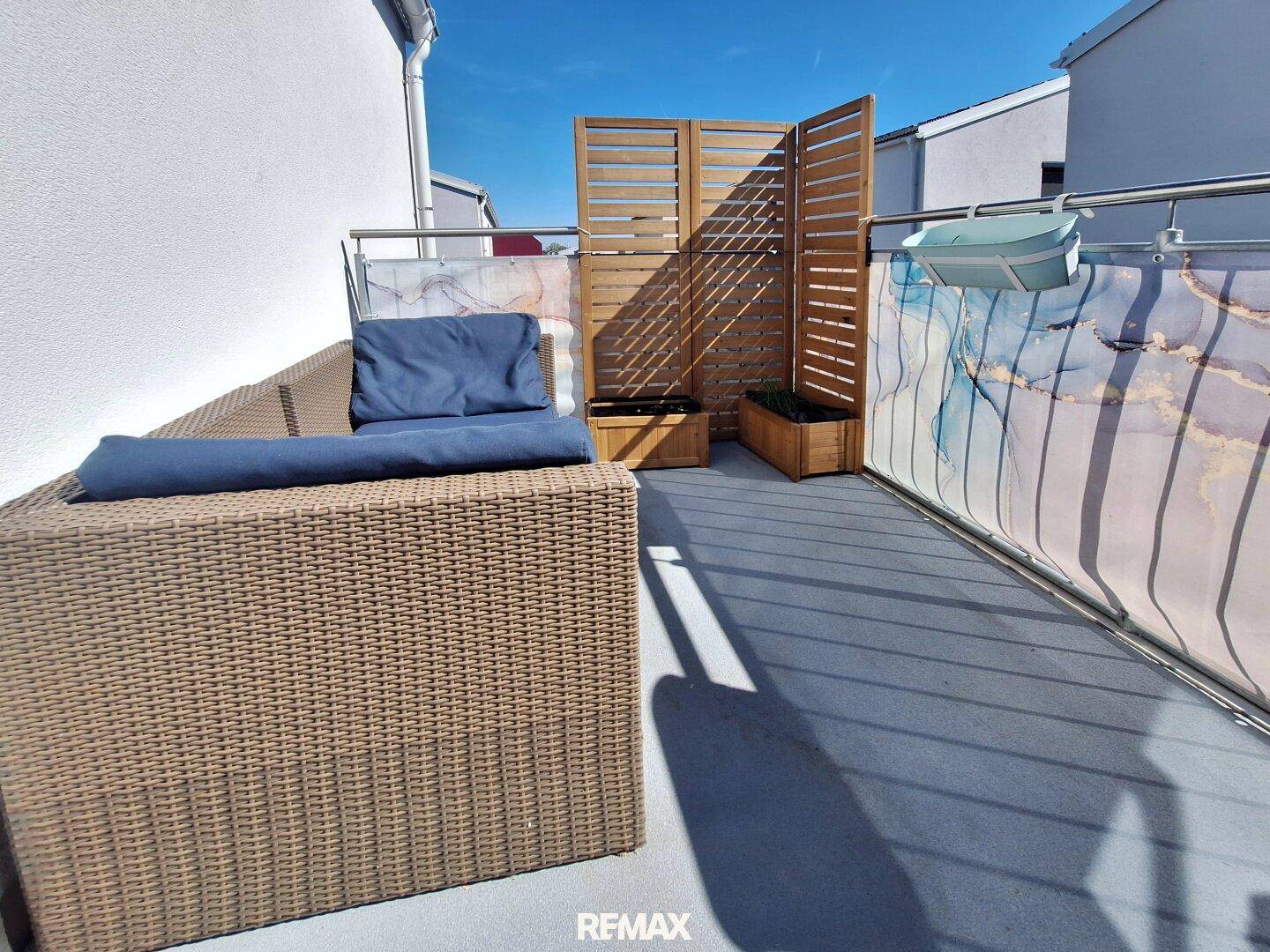 Sonniger Balkon mit Rattan-Sitzmöbeln und einem hölzernen Sichtschutz für Privatsphäre.