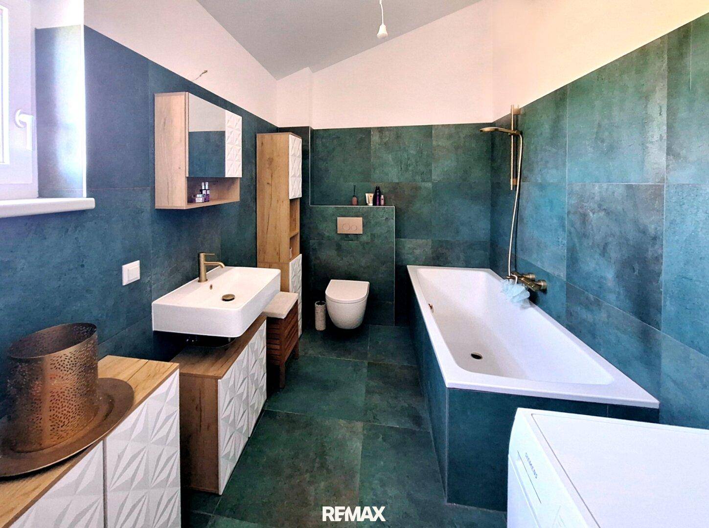 Modernes Badezimmer mit grünen Fliesen, Badewanne, Dusche und Holzmöbeln unter einer Dachschräge.