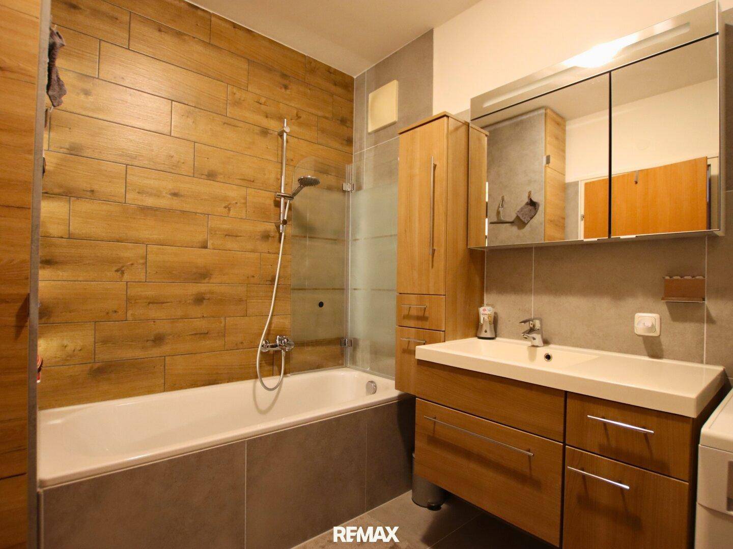 Badezimmer mit Badewanne, Duschfunktion und modernen Holzoptik-Fliesen an der Wand.