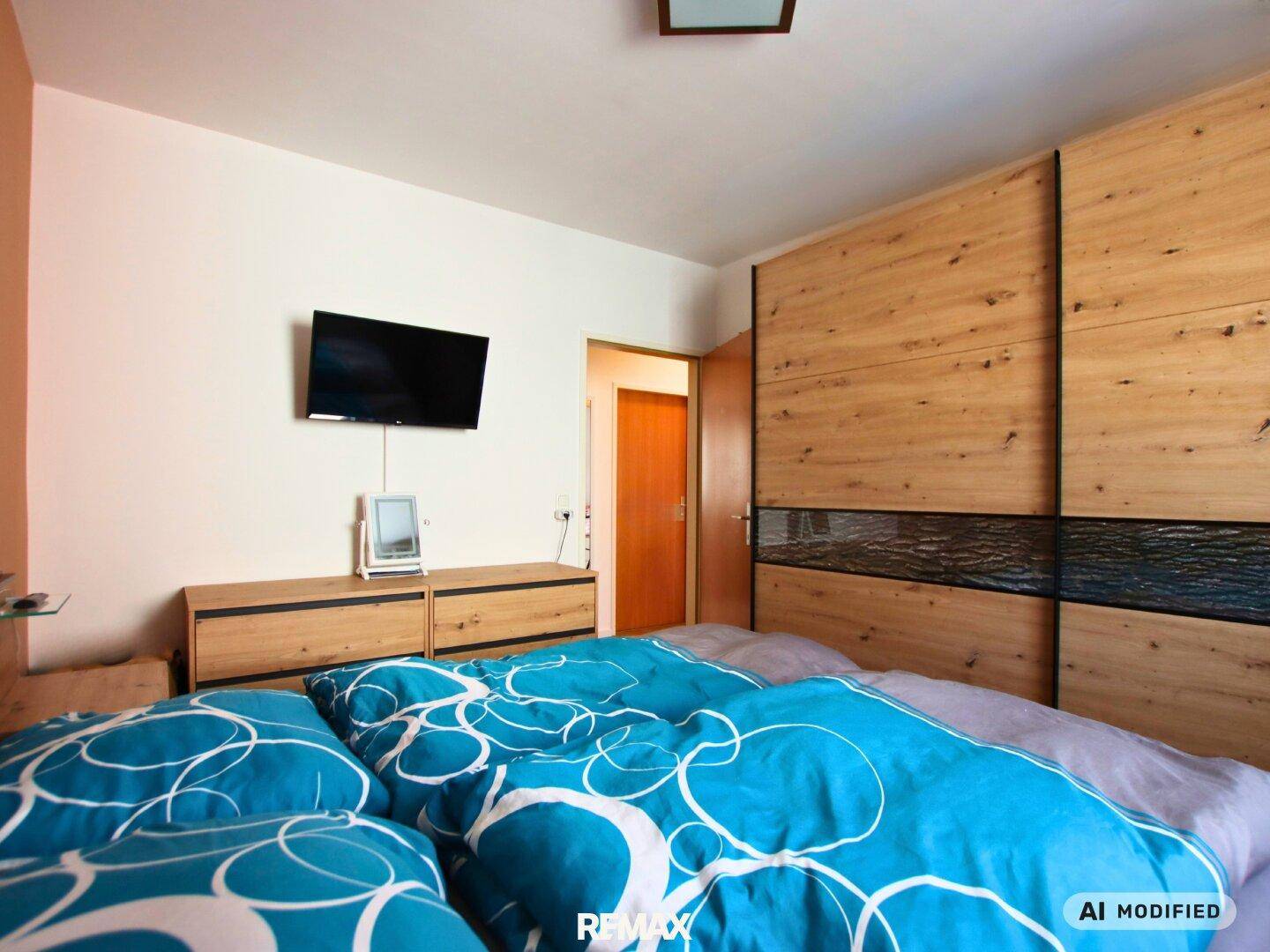 Schlafzimmer mit großem Holzschrank, Wandfernseher und komfortablem Doppelbett.