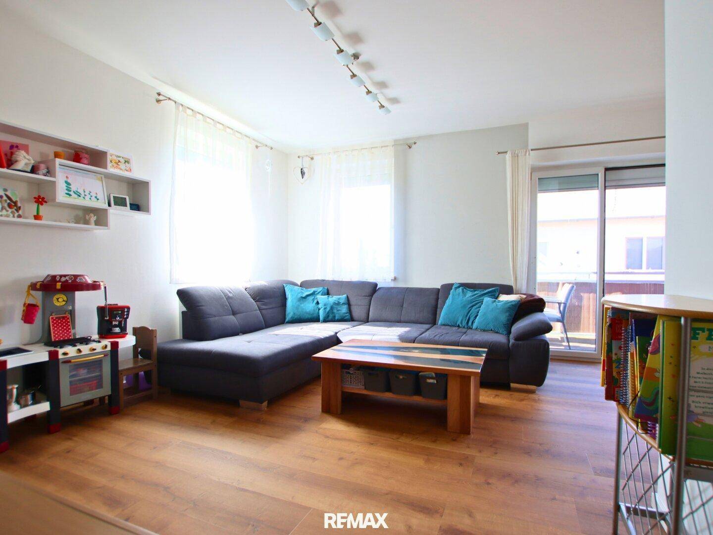Helles Wohnzimmer mit großem Ecksofa, Holzboden und Spielbereich für Kinder.