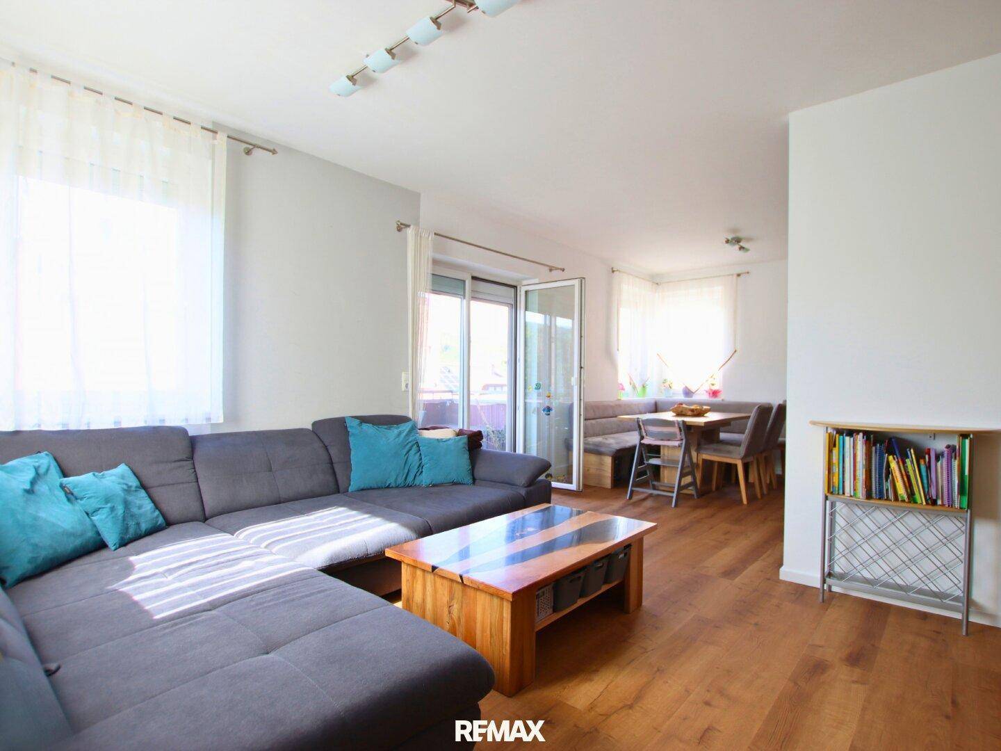 Geräumiger Wohn-Essbereich mit gemütlichem Sofa, Holzboden und Zugang zum Balkon.
