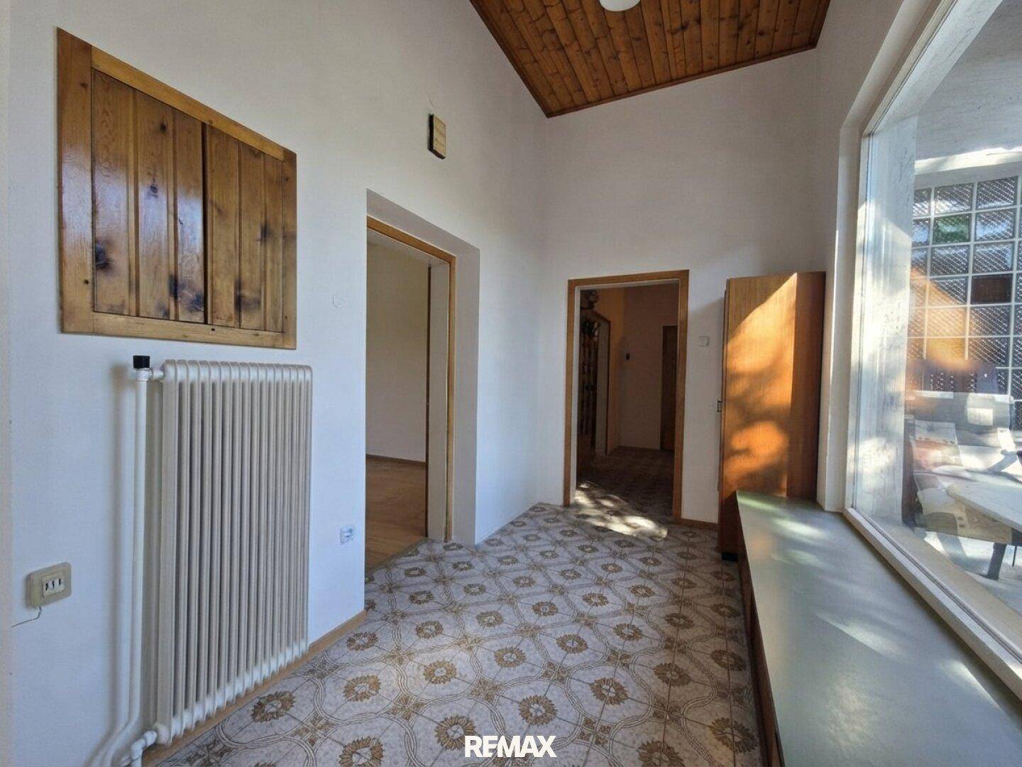 Flur mit Holzdecke, Heizkörper und Blick auf eine Glasbausteinwand im Außenbereich.