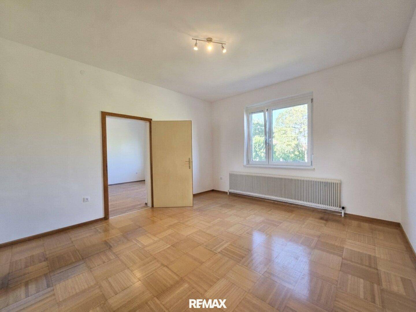 Helles Zimmer mit Parkettboden, großem Fenster und Blick ins Grüne.