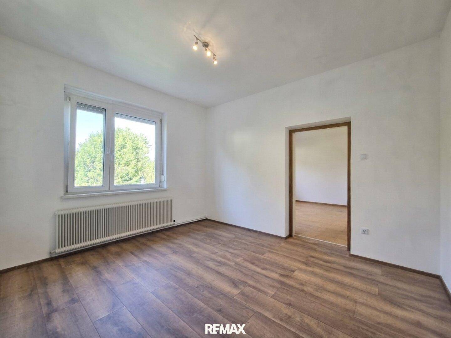 Geräumiges Zimmer mit Laminatboden, großem Fenster und viel Tageslicht.