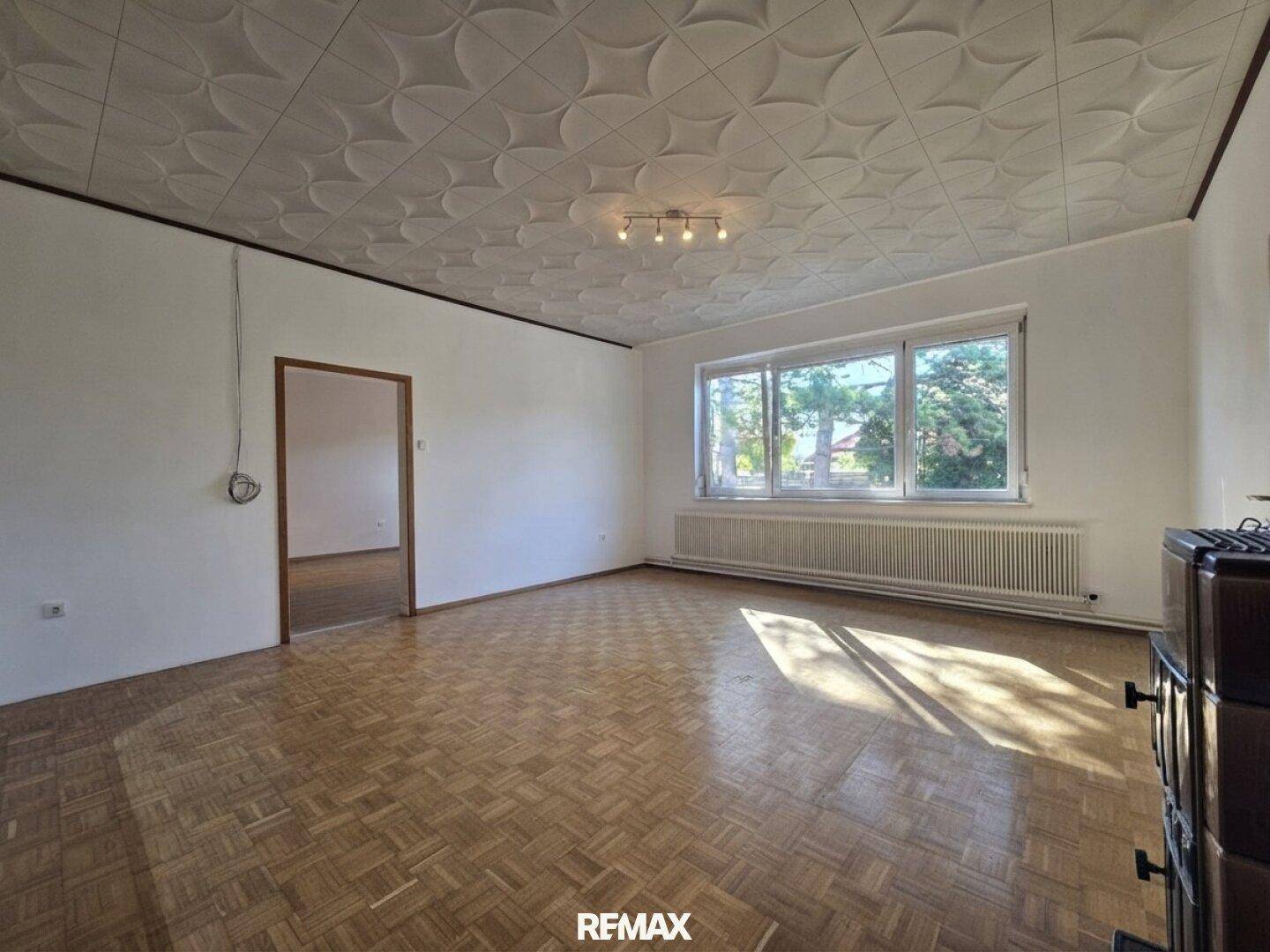 Geräumiges Wohnzimmer mit Parkettboden, dekorativer Decke und viel Tageslicht.