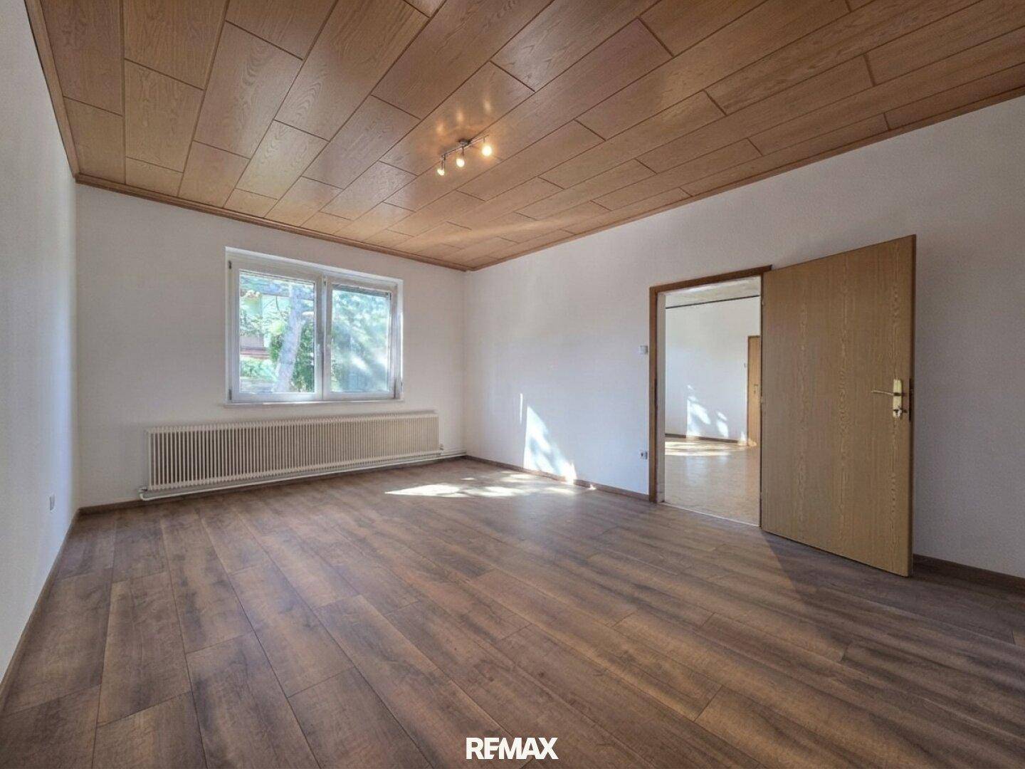 Helles Zimmer mit Laminatboden, Holzdecke und Fenster mit Blick ins Grüne.