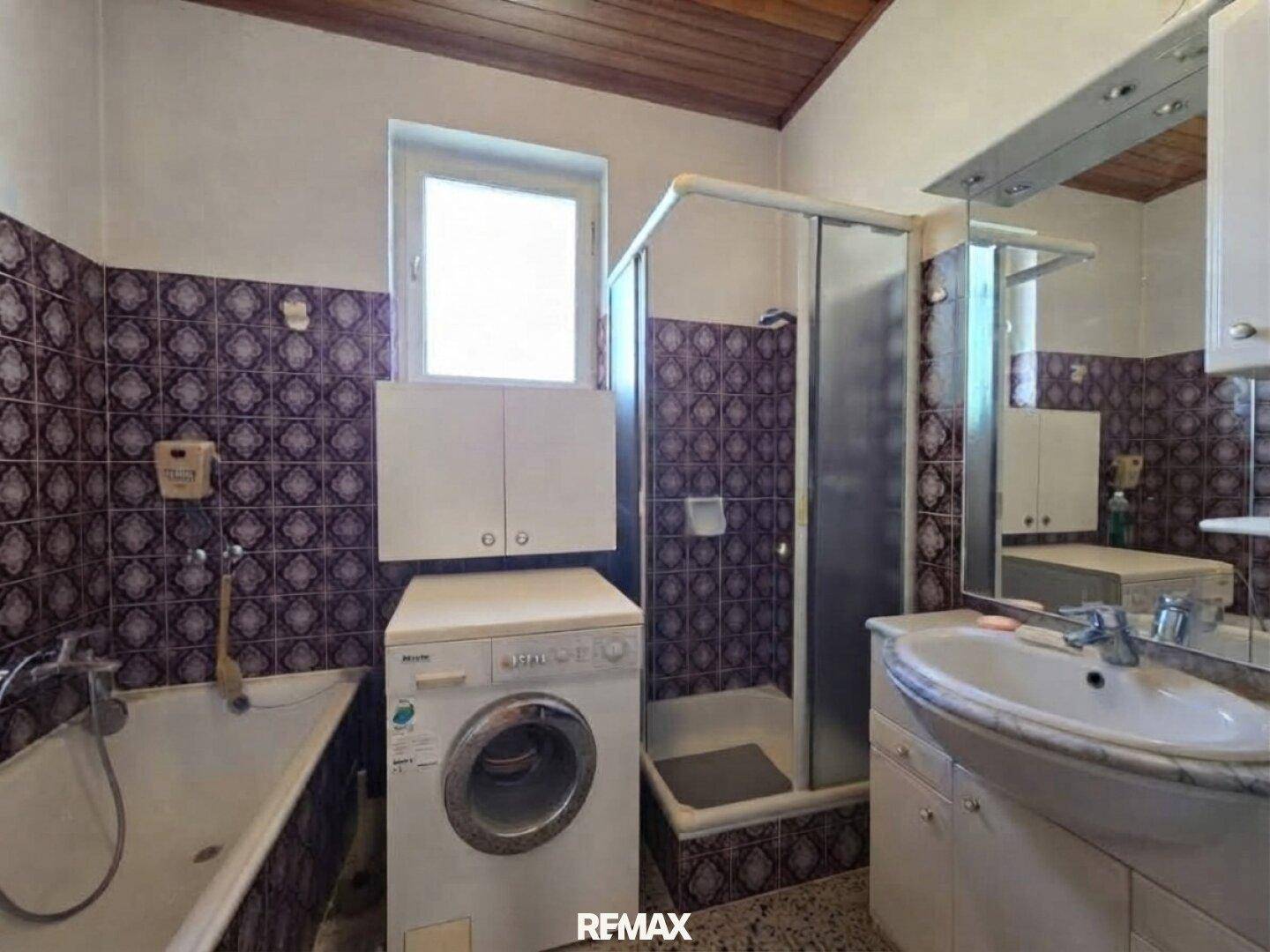 Badezimmer mit Badewanne, Duschkabine, Waschbecken und Waschmaschine, ausgestattet mit gemusterten Fliesen.
