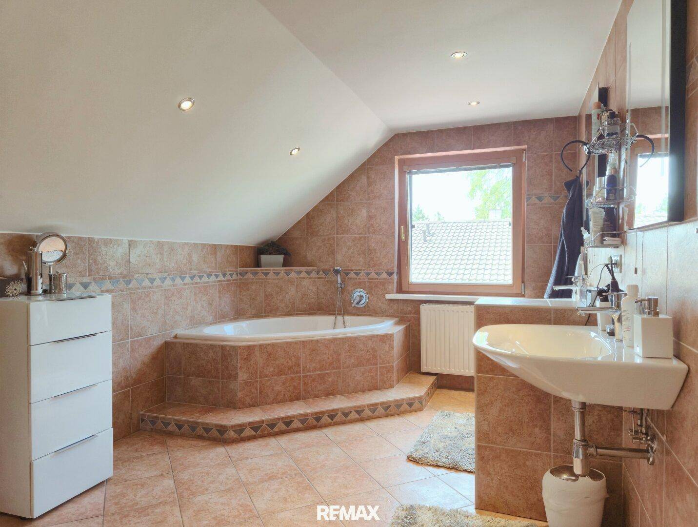 Geräumiges Badezimmer im Dachgeschoss mit Eckbadewanne, Fliesen und Fenster.