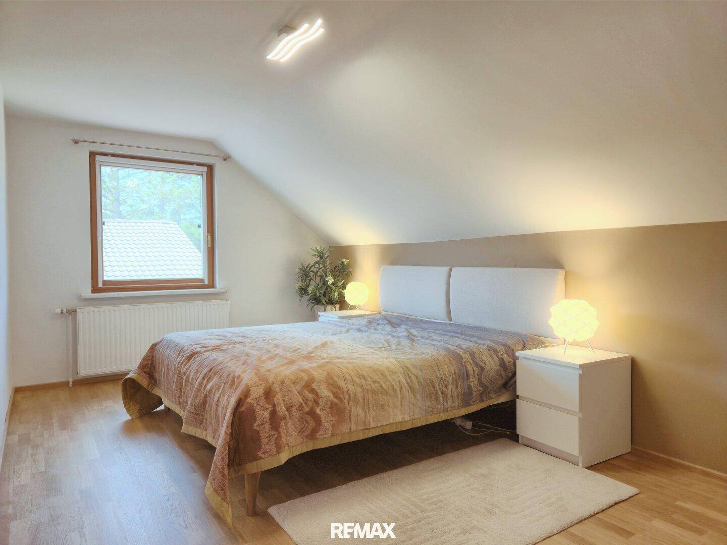 Helles Schlafzimmer mit Doppelbett, Holzboden und Fenster.