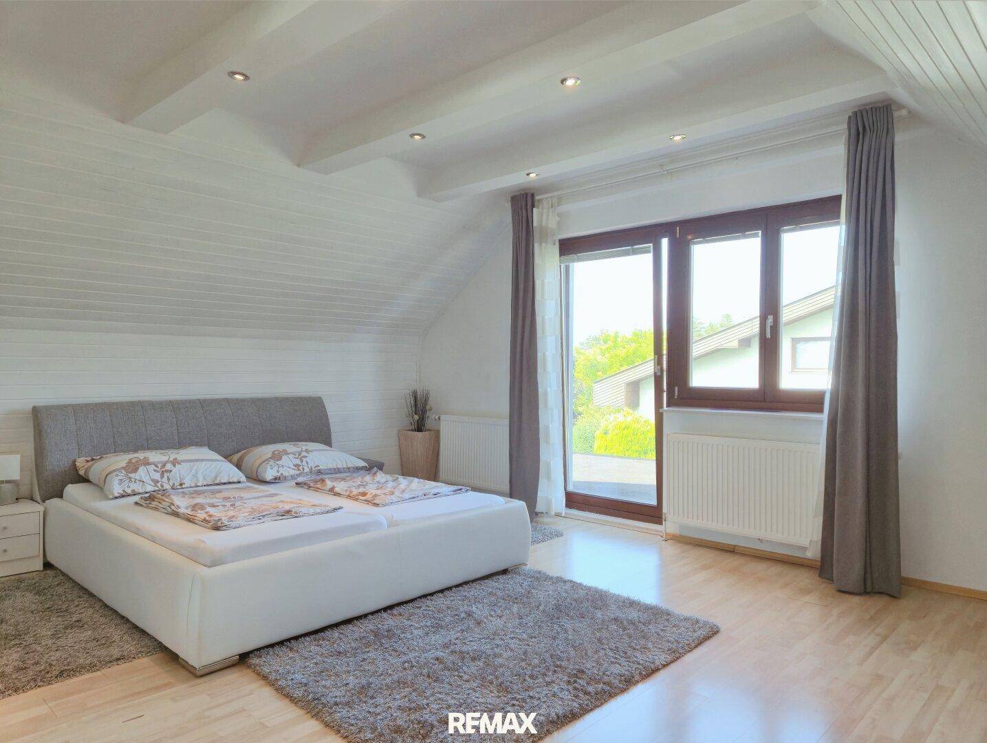 Schlafzimmer mit Doppelbett, Holzboden, Dachschrägen und Zugang zum Balkon.
